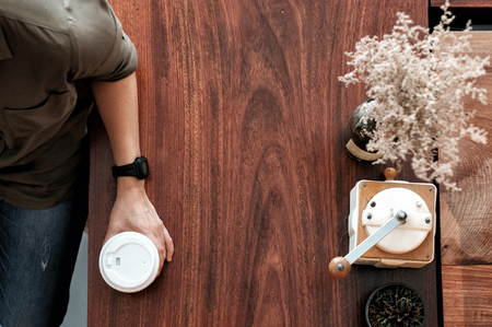 Hand holding take away coffee cup on wooden table at cafe background, top view with copy spaceの写真素材