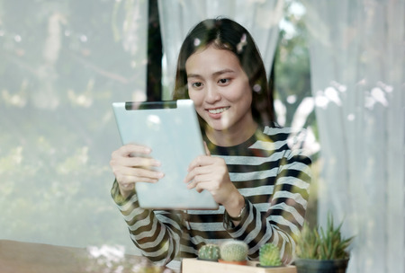 Young asian woman using tablet while sitting by window cafe backgroundの写真素材