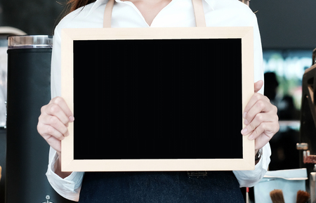 Young asian women Barista holding blank chalkboard menu with smiling face at cafe counter background, small business owner, food and drink industry conceptの写真素材