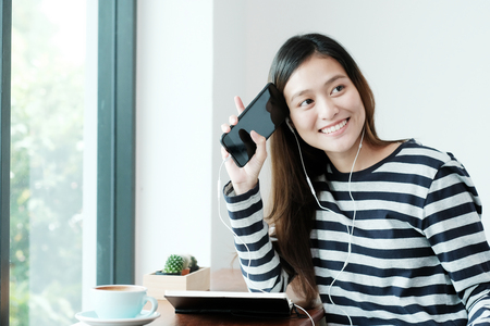 Young asian woman using smart phone with earphones at cafe background, People on phone and lifestyleの写真素材
