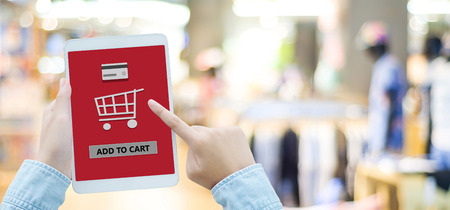 Hand holding tablet with online shopping device on screen over blur store background, banner with...