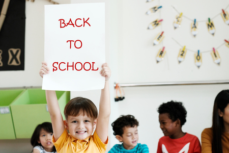 Cute boy holding back to school poster with happy face in kindergarten classroom, education conceptの写真素材