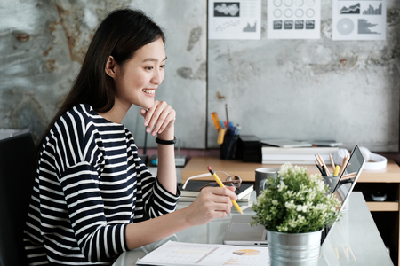 Young asian businesswoman working at office table with smiling face, positive emotion, casual office life conceptの写真素材