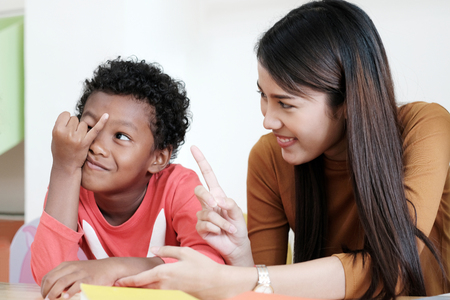 Young asian woman teacher teaching american african kid in kindergarten classroom with happiness and relaxation, kid education conceptの写真素材