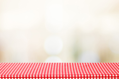 Empty table covered with red check tablecloth over blurred cafe with bokeh light background, product, food display montageの写真素材