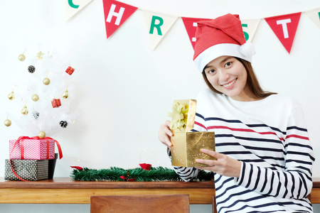 Young cute asian woman wearing santa hat smiling while holding golden Christmas gift box, Christmas people celebration conceptの写真素材