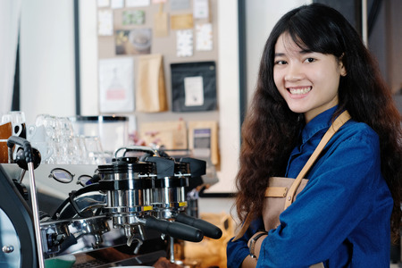 Young asian woman Barista standing with smiling face in font of cafe counter background, small business owner, food and drink industry conceptの写真素材