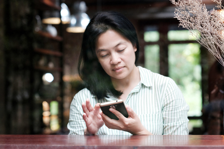 Asian woman using smart phone sitting by window cafe background, People communication technology and lifestyleの写真素材