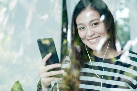 Asian woman using smart phone sitting by window cafe background
