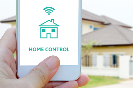 Hand using smart phone as smart home control application over blurred house background, banner, smart home concept, the internet of thingsの写真素材