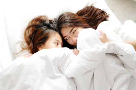 Young cute asia lesbians lying on white bed together in the morning, LGBT, couple lesbians conceptの写真素材