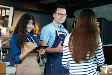 Young asian barista taking customer order at coffee cafe counter with smiling face, food and drink business conceptの写真素材