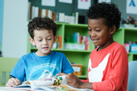 American and African boys are reading together with happiness in their kindergarten classroom, kid education and diversity conceptの写真素材