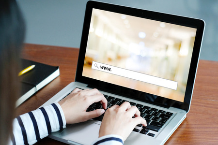 Hand tying labtop computer with www. on search bar over blur store background on screen, on line shopping ,business, E-commerce, technology and digital marketing concept backgroundの写真素材