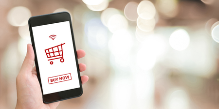 Hand holding smart phone with shopping online device on screen over blue background with copy space, business and technology, online shopping conceptの写真素材