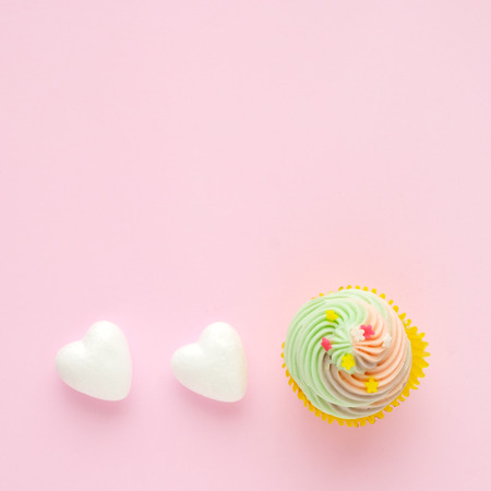 Pastel cupcake and white hearts on pink background with copy space for text, birthday, anniversary greeting card background, flat lay, top viewの写真素材