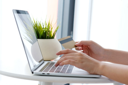 Young asian woman holding credit card and using laptop computer for shopping on line at cafe,...