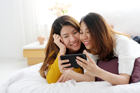Young cute asia lesbian couple using smart phone with happiness at home, lgbt, homosexual, lesbian couple lifestyleの写真素材