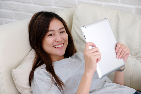 Young asian woman using tablet with smiling, happy and relax emotion on sofa in white room background, people and technology, lifestyleの写真素材