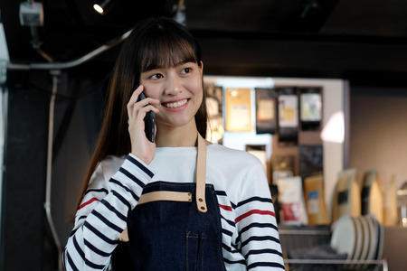 Young asian woman barista taking phone while working at cafe, food and drink, samall business and modern workplace conceptの写真素材