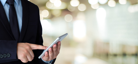 Businessman using smart phone over blur office background with copy space for text, people on phone, technology and lifestyleの写真素材