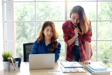 Two young asian women working with laptop computer at home office with happy emotion, working from home, small business, office casual lifestyle conceptの写真素材