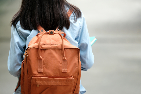 Back of student girl holding books and carry school bag while walking in school campus background,...