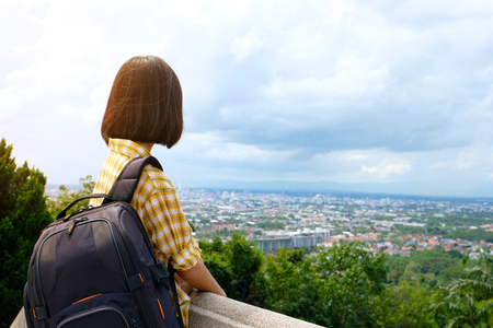 Back of young asian girl traveler standing in city and outdoors nature view background, travel spring, summer holiday vacation concept, gen Zの写真素材