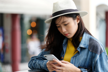 Young asian woman using phone standing in front of cafe in the city outdoors background, people working outdoors with technology, lifestyleの写真素材