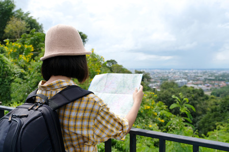 Young asian girl traveler standing with backpack and map while traveling in countryside outdoor, people spring and summer holiday vacation background conceptの写真素材