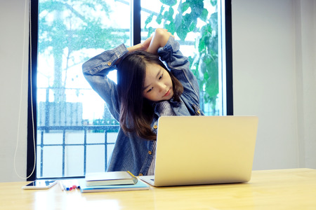 Young asian woman stretching body for relaxing while working with laptop computer at her desk, office lifestyle, business situationの写真素材