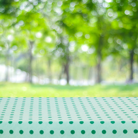 Empty table with green and white tablecloth over blurred park nature background, for product display montage, spring and summerの写真素材