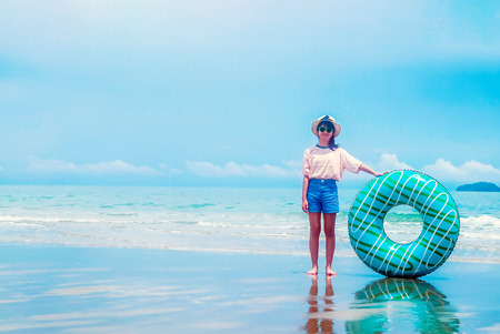 Cute asian girl on summer sea beach holding swim ring, wearing hat, eyeglasses and smiling with happiness, people on summer holiday vacationの写真素材