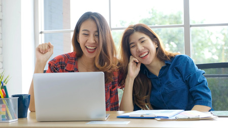 Two young asian women working with laptop computer at home office with happy emotion moment, working at home, small business, office casual lifestyle conceptの写真素材