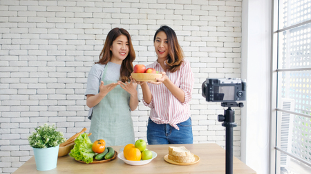 Two young asian women food bloggers talking while recording video with happy moment, vlog concept, people and technology communicationの写真素材