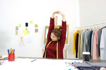 Young asian woman fashion designer stretching body for relaxing while working in home studio, small business owner, fashion industry conceptの写真素材