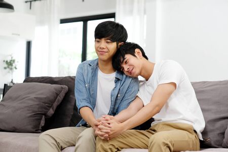 Young asian gay man couple holding hands with happiness while sitting in home living room, homosexual and lgbt lifestyle conceptの写真素材