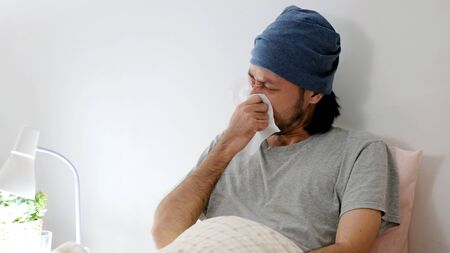 Asian man blowing nose with  tissue whle lying on bed at night, Asia male get sick with flu,...