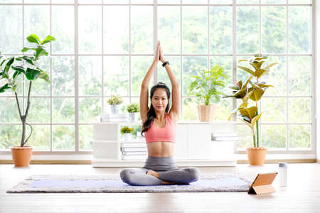Asian woman practice yoga meditation exercise at home, Young asia female sitting on mat for relaxed yoga posture in the morning , exercise at home, wellbeing, mental health careの写真素材