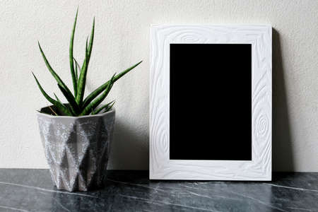 Empty white vintage wooden frame standing over white cement wall and black marble floor with shadow...