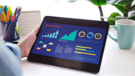 Man hand holding digital tablet with analyze data and business growth on device screen at home...