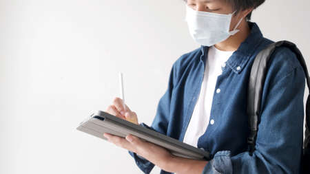 Young asian university student using digital tablet for online learning while wearing protection...