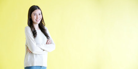 Happy asian woman arm cross, smiling and looking at camera while standing over isolated yellow background with copy space, Portrait of asia femaleの写真素材