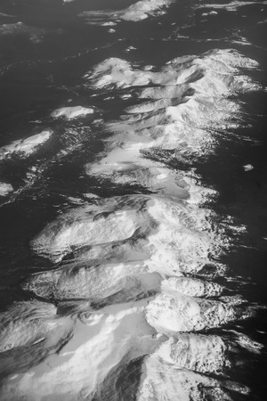 The surface of the Earth from the airplane window. The mountains are covered with snow. Black forest...