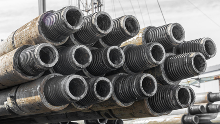 Drill pipes for drilling oil and gas wells are located horizontally on the rack. In the foreground is a threaded pipe joint. In the background is a blurred image of the other pipes.の写真素材