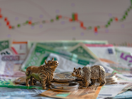 Bronze figures of a bull and a bear near metal coins against the background of paper money and the diagram of a trading terminal. Blur background and perspective. Concept and symbol of stock exchange and stock trading.の写真素材