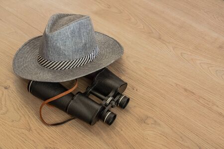 Wide-brimmed gray hat and binoculars, as symbols of travel. Wooden yellowish background. Preparation for the designer. Copy space.の写真素材
