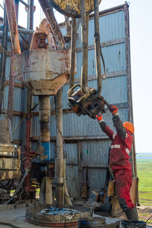 Gydan Peninsula / Russia - August 8 2019: Work driller in red uniform, in helmet and goggles. He with the help of an elevator hangs drill pipes to lift them from an oil well and continue its drilling. The concept of a working person.のeditorial素材