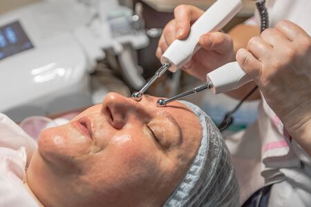 A cosmetic procedure with microcurrent injections in a beauty salon is performed for an aged woman. Improving skin turgor, rejuvenation and healing.の写真素材