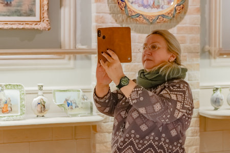 Moscow / Russia - February 18 2020: A woman with a smartphone photographs the exhibits of an antique exhibition of ceramics and porcelain in Breton style.のeditorial素材